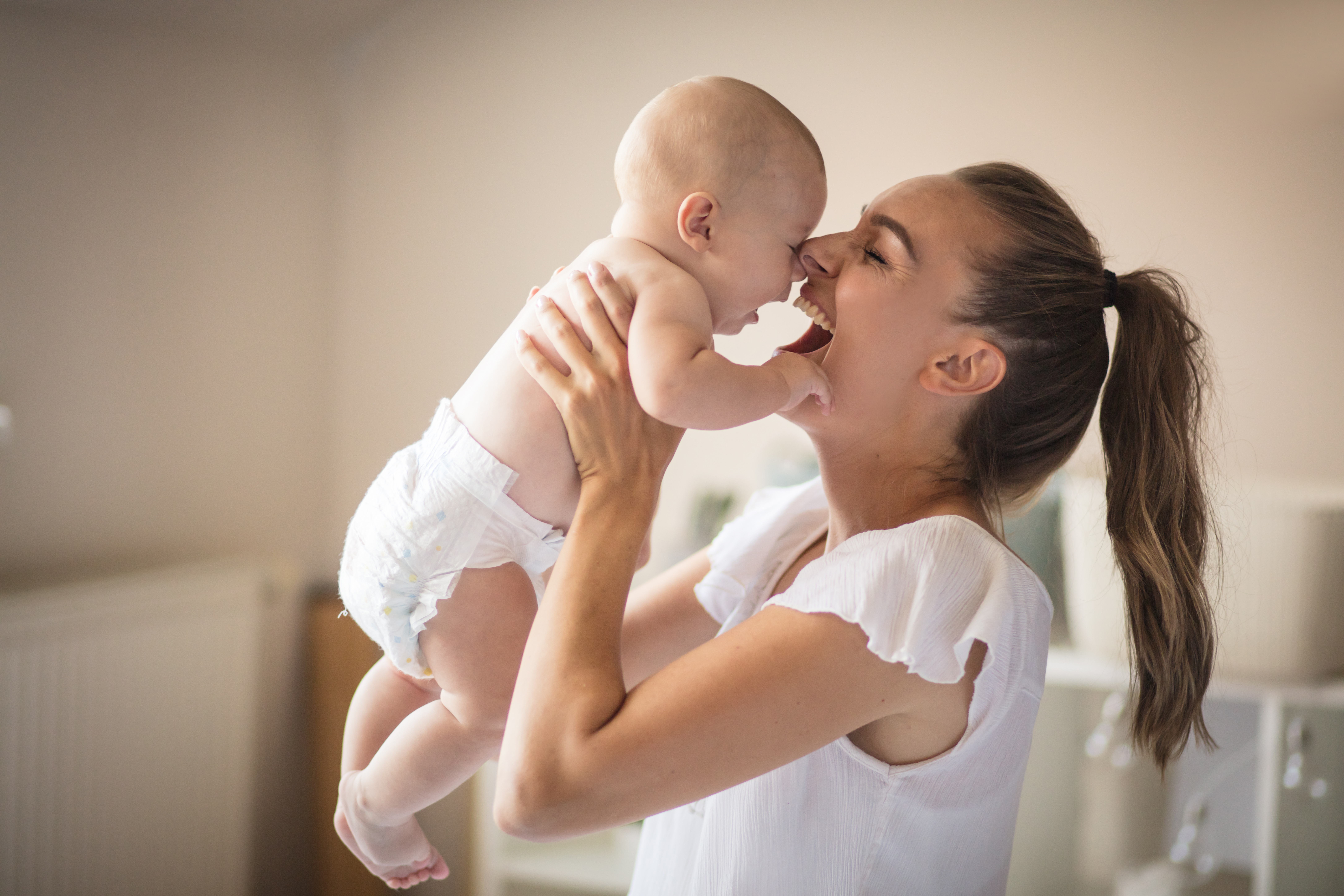 Young mom playfully lifting small baby up in the air