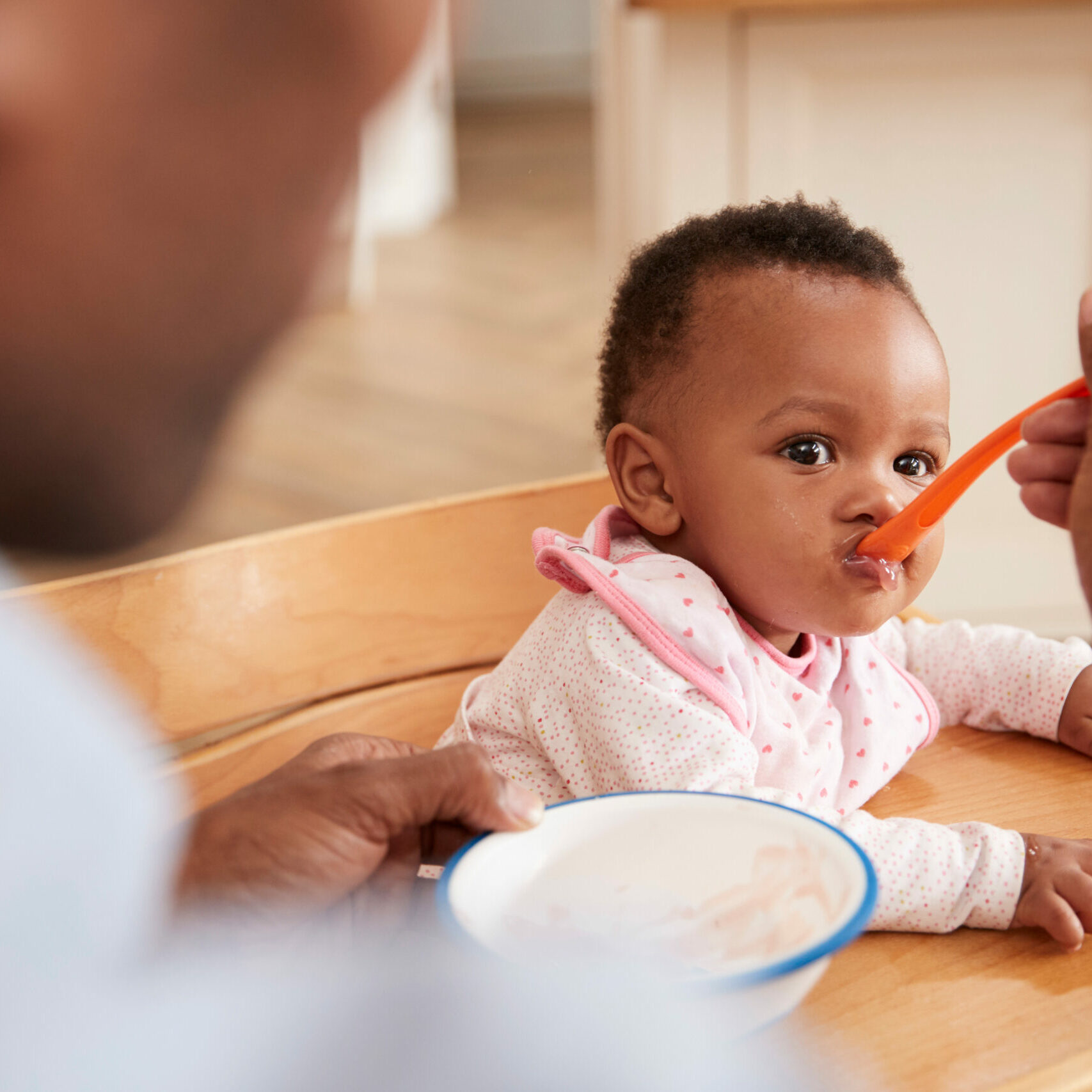 Baby in high chair being fed with a spoon by a parent