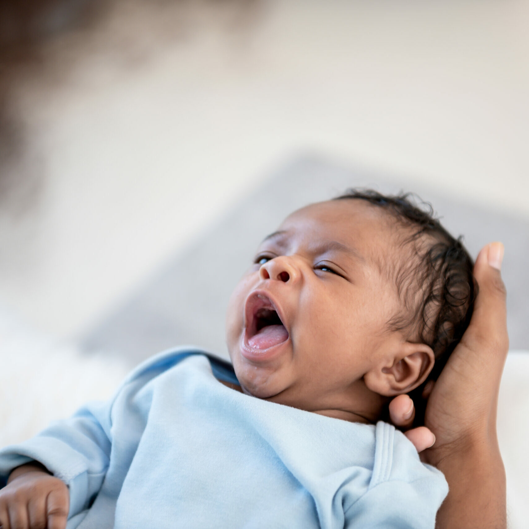 1 month old baby is yawning sleepy while lying on the palm of his mother