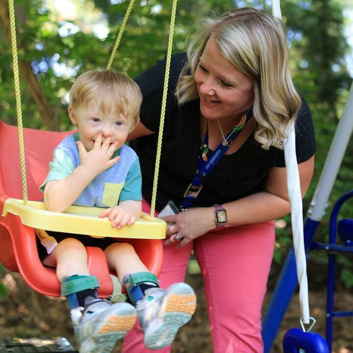 Joyful toddler in a safety swing with adult assisting