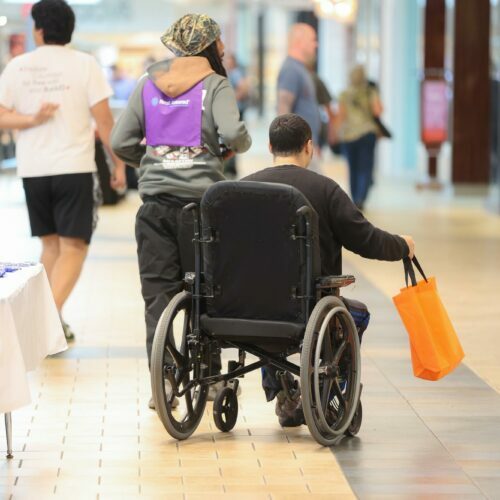 image of man in a wheelchair from behind holding an orange bag