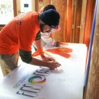 Man in orange shirt signing Summit DD "I Heart Inclusion" banner at Inclusion Days at the Zoo event